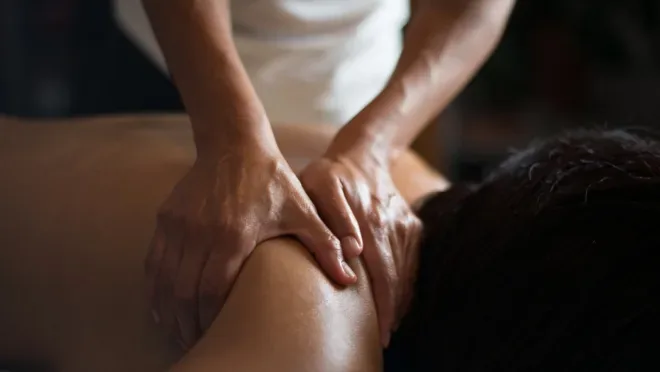 Therapist's hands pressing and massaging a person's shoulder and upper back during a massage session