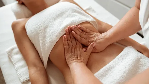 Therapist's hands performing an abdominal massage on a relaxed person lying on a towel-covered table with a towel over chest.